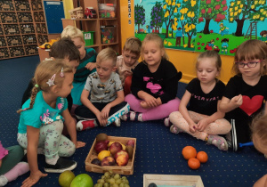 Dzieci siedzą na podłodze w klasie i klasyfikują owoce.