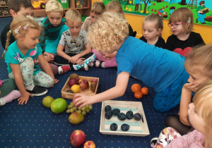 Dzieci siedzą na podłodze w klasie i klasyfikują owoce.