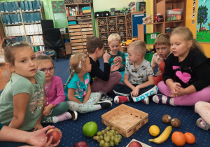Dzieci siedzą na podłodze w klasie i oglądają owoce.