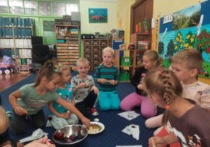 Dzieci siedzą na podłodze w klasie i smakują owoce.