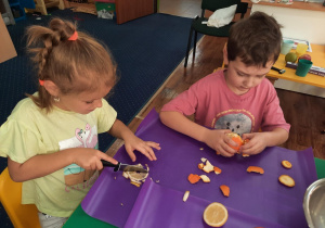 Dzieci siedzą przy stole i przygotowują owoce na sałatkę.