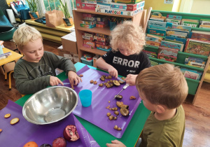 Dzieci siedzą przy stole i kroją owoce na sałatkę.