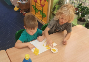 Chłopcy siedzą przy stole i stemplują palcami z wykorzystaniem farb kształt prostokąta.