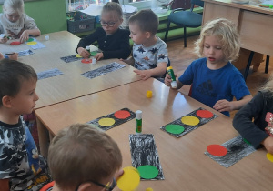 Dzieci siedzą przy stole i naklejają kolorowe koła na sygnalizatorze świetlnym.