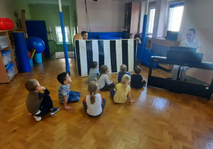 Dzieci siedzą przed pianinem i śpiewają piosenkę o ruchu drogowym.