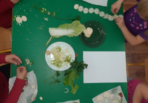 Dzieci przy stole wykonują kompozycje z warzyw.