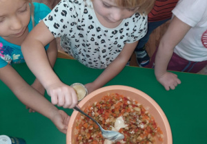 Dziewczynka wkłada do miski z sałatką majonez.