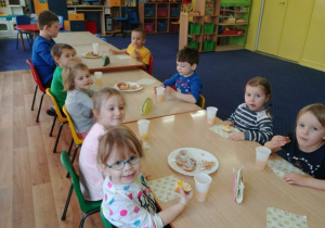 Dzieci przy stolikach jedzą faworki i pączki.