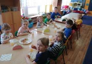 Dzieci przy stolikach jedzą faforki i pączki.