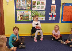 Dziewczynka siedzi na krześle z cukierkami, a pozostałe dzieci w kole na dywanie.
