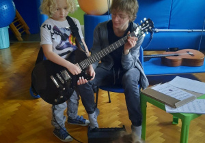 Chłopiec próbuje grać na gitarze elektrycznej.