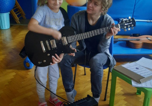 Dziewczynka próbuje grać na gitarze elektrycznej.