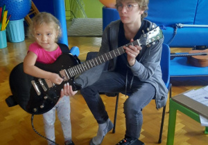 Dziewczynka próbuje grać na gitarze elektrycznej.