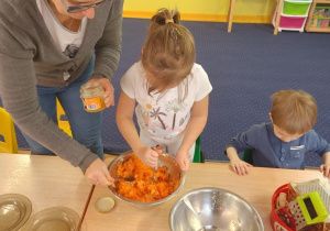 Dzieci siedzą przy stole i trą marchewkę.