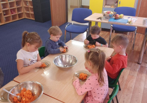 Dzieci siedzą przy stole i zjadają surówkę z marchewki.
