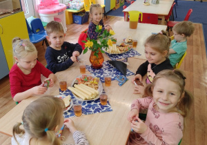 Dzieci siedzą przy stole na którym stoją słodkości i napoje.