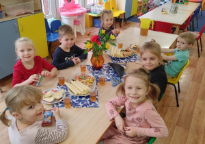 Dzieci siedzą przy stole na którym stoją słodkości i napoje.