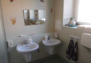 Łazienka. Na zdjęciu widać dwie umywalki nad którymi znajduje się lustro. Obok umywalek wiszą dwa ręczniki.